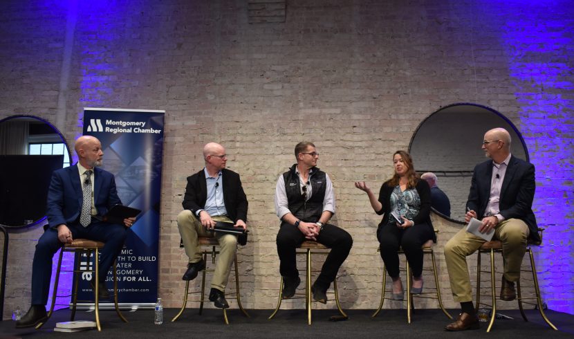 This is a photo of four people sitting in chairs. The only women in the picture is speaking.