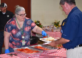 A woman puts a slice of tomato on a man's plate