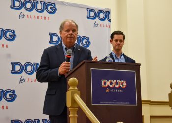 This is a picture of Doug Jones speaking on a stage with Phillip Ensler behind him