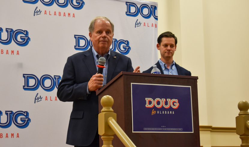 This is a picture of Doug Jones speaking on a stage with Phillip Ensler behind him