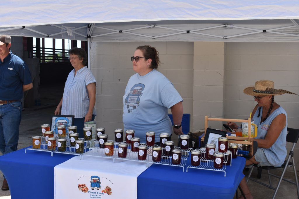 This is a picture of a woman standing behind a table with jars on it under a tent
