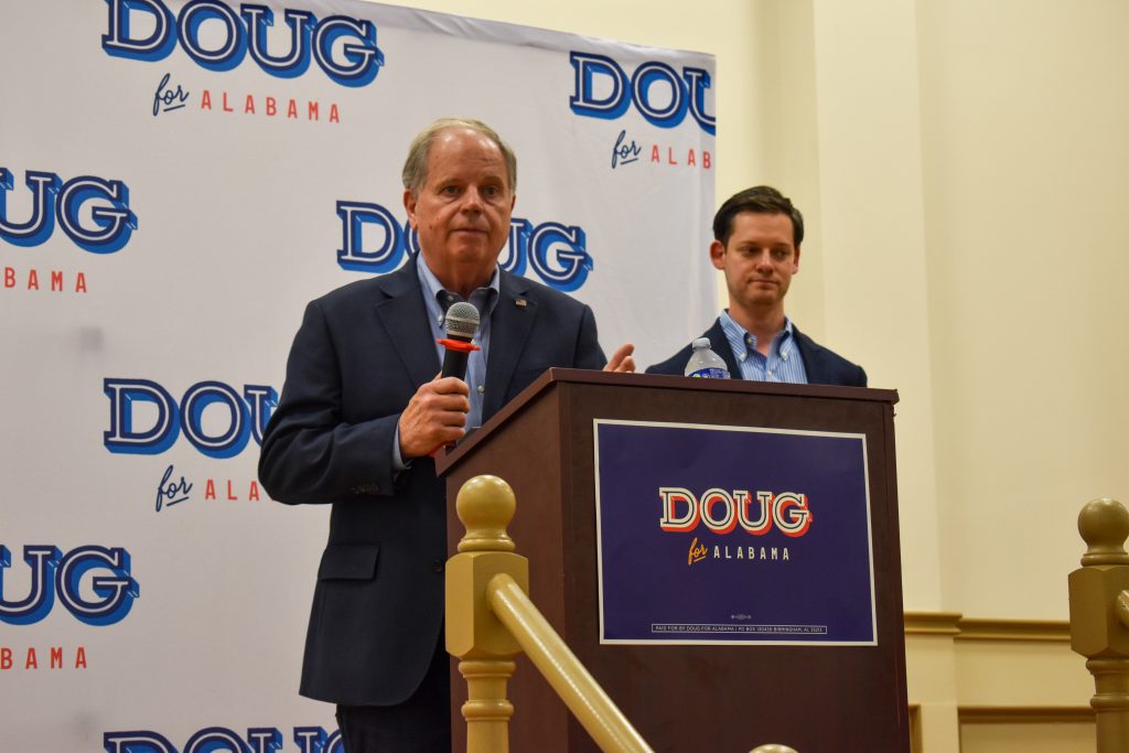 This is a picture of Doug Jones speaking on a stage with Phillip Ensler behind him